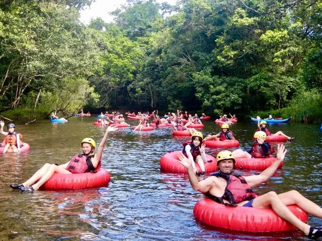 Many people floating on red tubes down a river surrounded by lush forest.
