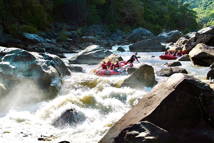 Several yellow rafts with people navigating through rocky river rapids.